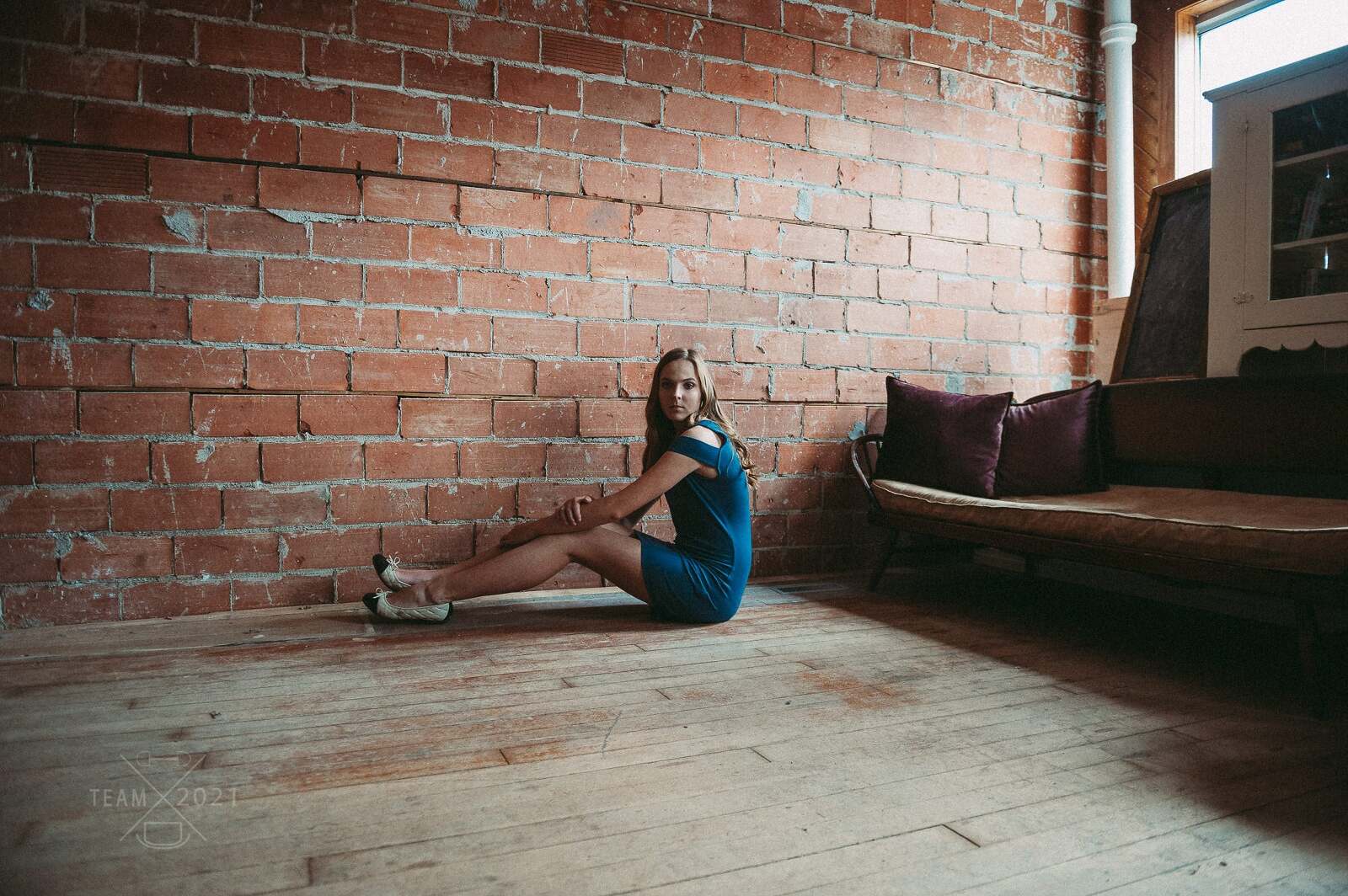 teenage girl sits on the floor in front of a brick wall